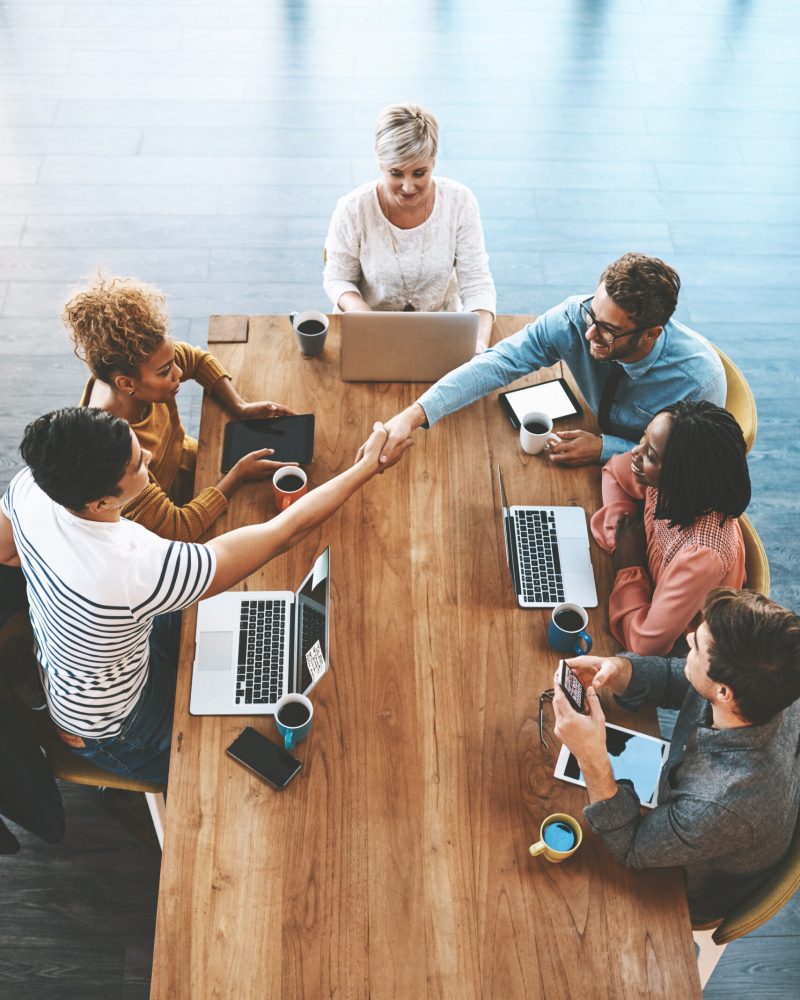 Handshake, above and business people in a meeting at work for onboarding and welcome. Happy, interview and corporate employees shaking hands for thank you, deal or partnership in a group discussion.